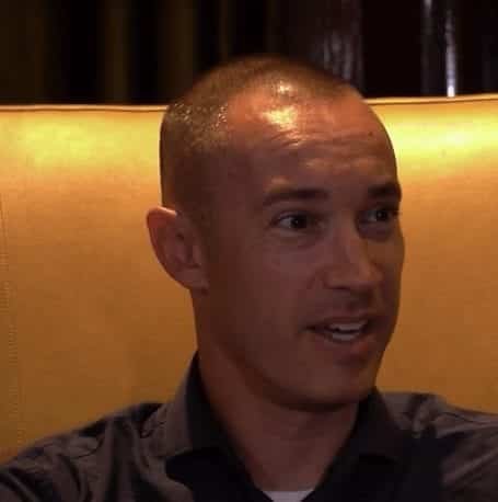 A man with short hair and a dark shirt sits on a tan chair speaking with a dark background behind him | edCircuit A man with short hair and a dark shirt sits on a tan chair speaking with a dark background behind him