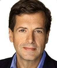 A middle-aged man with short brown hair, wearing a blue shirt and dark jacket, looking directly at the camera with a neutral expression in front of a plain white background.