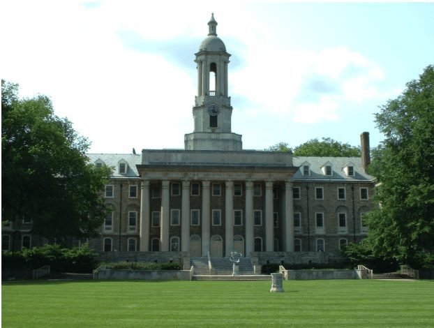 Historic university building with tall columns and a clock tower behind a wide lawn and trees