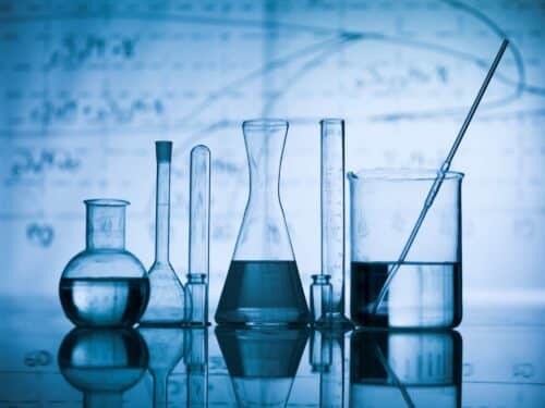 Group of laboratory flasks empty or filled with a clear liquid on blue tint scientific graphics background and their reflection on a table