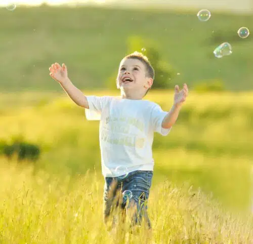 child chasing bubbles in field