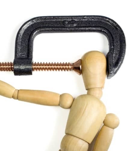 A clamp squeezing tightly on the head of a wooden man.