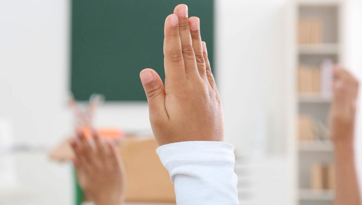 Children raising hands up in classroom