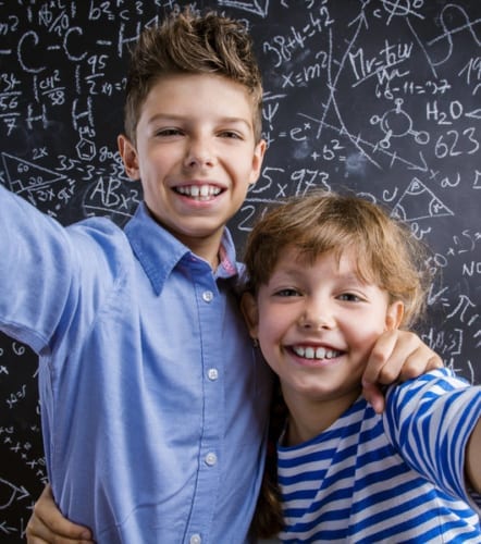 Two kids smiling in front of a blackboard
