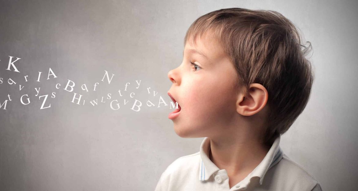 A young boy in a white shirt is shown in profile, speaking with illustrated letters emerging from his mouth, symbolizing speech or communication. The background is plain and gray.