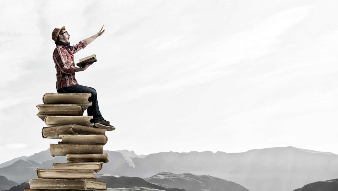 man sitting on books near mountains