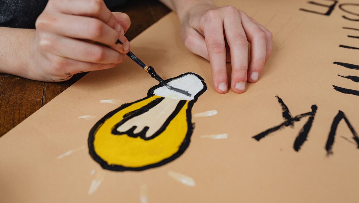 A hand painting a light bulb illustration on paper for a school project
