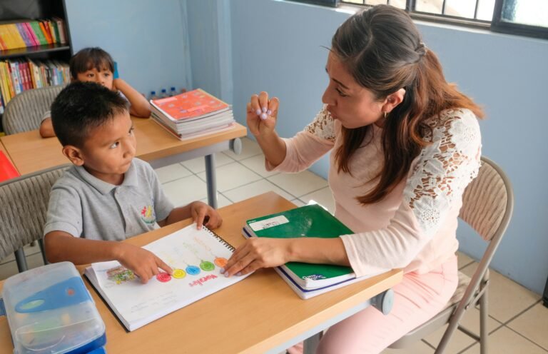 A teacher gesturing to a student pointing at a colorful workbook in a
