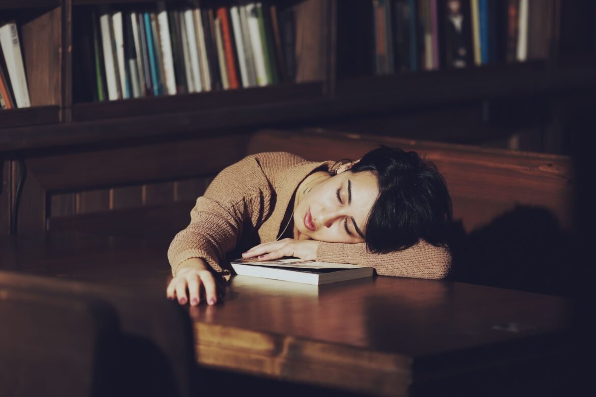 A woman with short hair sleeps on a table in a quiet library, resting