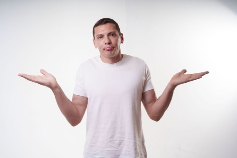 Adult man in white t-shirt shrugs in studio, expressing confusion agai