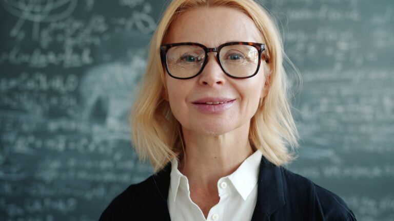 A woman with glasses in front of a chalkboard