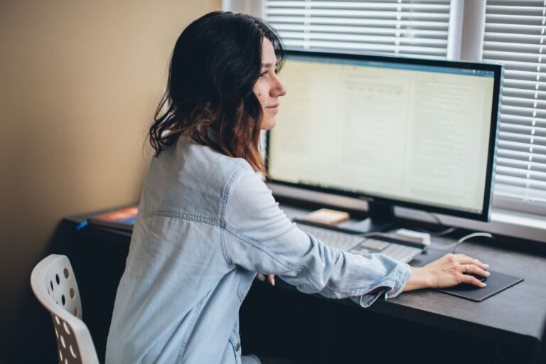 A woman working remotely from her home office desk using a computer mo