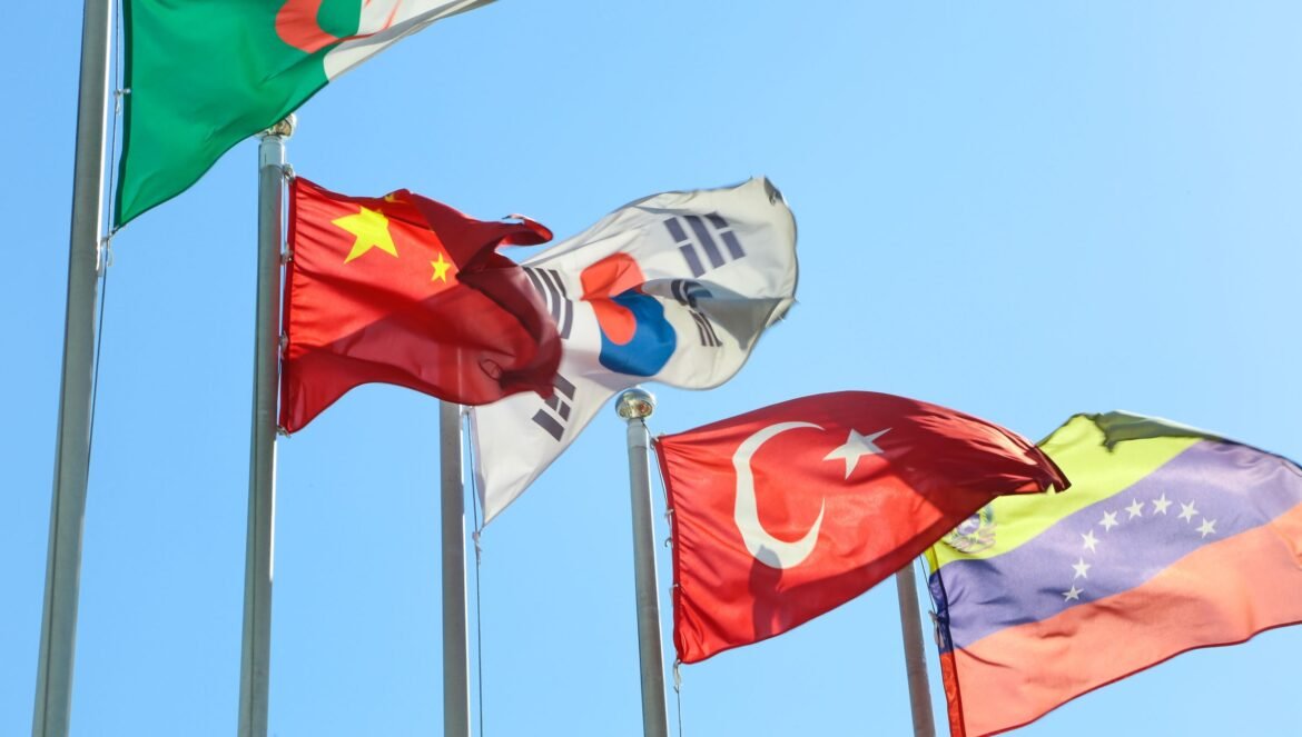 Five national flags from different countries waving on flagpoles under