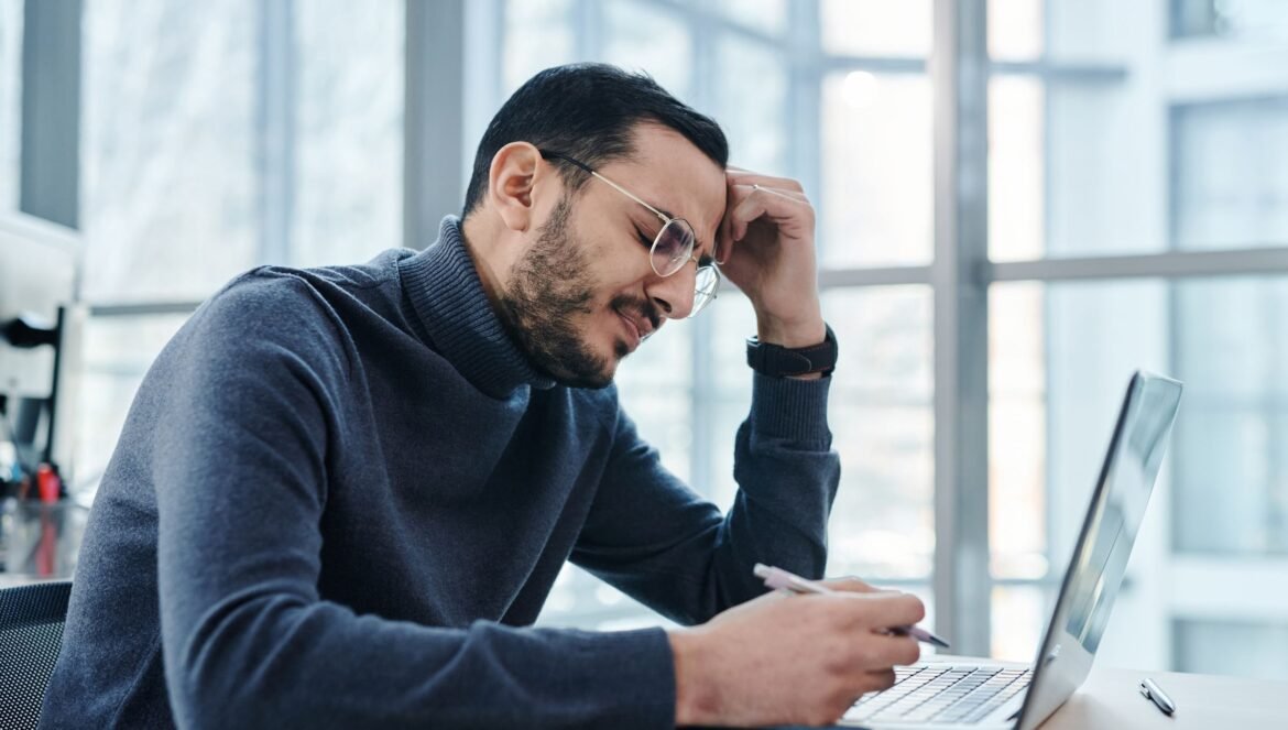 Man looking stressed at laptop in a modern office with large windows | edCircuit Man looking stressed at laptop in a modern office with large windows