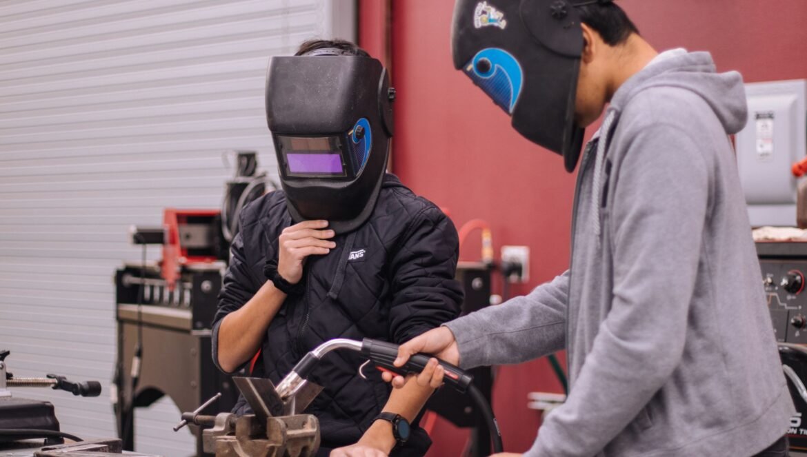 Two welders in protective gear concentrate on a project in a workshop