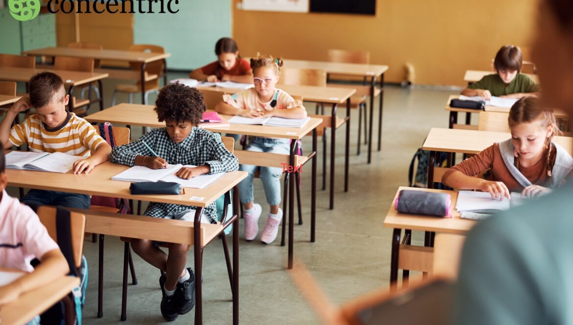Students sit at desks in a classroom, working on assignments or tests, with a teacher standing in the foreground and the word concentric in the top left corner.