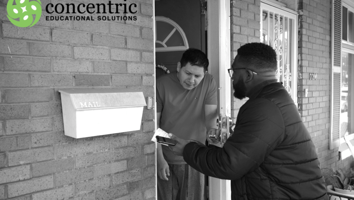 A man stands at a front door speaking with another man who is holding a phone and a paper; a mailbox and concentric educational solutions logo are visible.