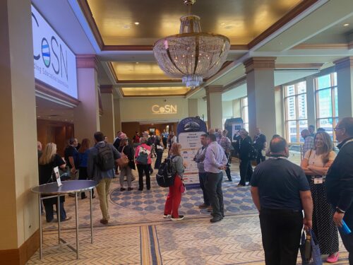Attendees gather and network in a hotel lobby at a CoSN event, with a chandelier overhead and CoSN signage visible in the background.