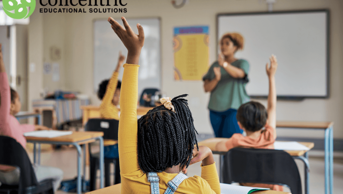 Students raise their hands in a classroom as a teacher stands at the front; Concentric Educational Solutions logo in the top-left corner.