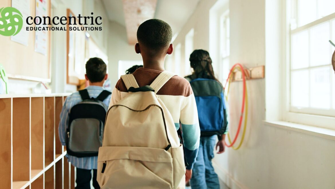 Students with backpacks walk down a bright school hallway concentric educational solutions logo appears in the top left corner