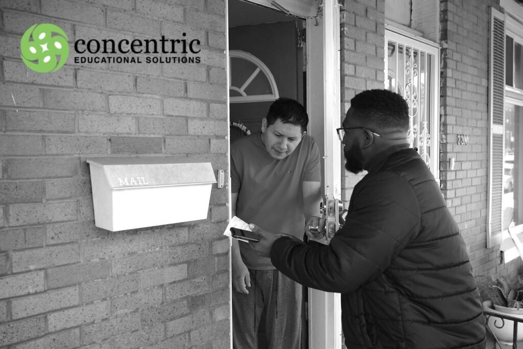 Two men at a brick doorstep exchange a small parcel one hands it to the other inside an open door with a Concentric Educational Solutions logo in the corner