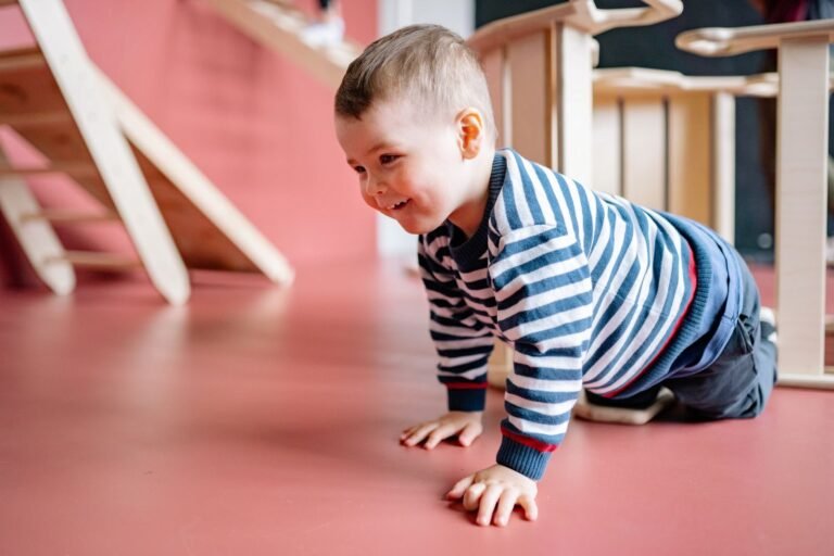 A cheerful toddler in striped long sleeves crawls on a red floor indoo