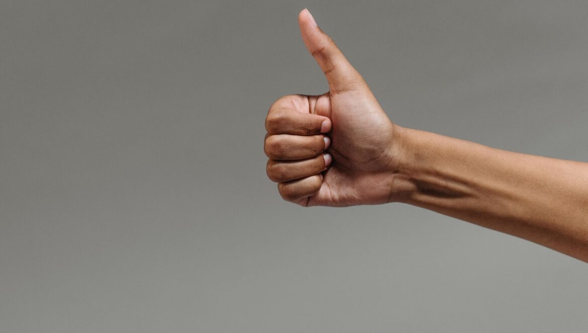 A close up image of a hand making a thumbs up gesture against a neutral background