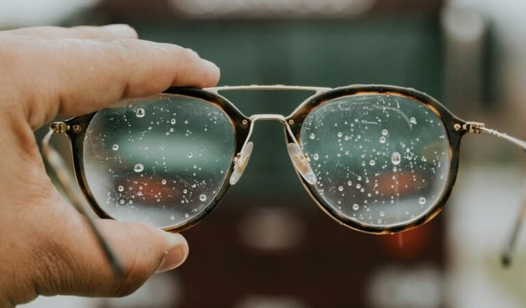 A hand holding a pair of glasses with water droplets on it