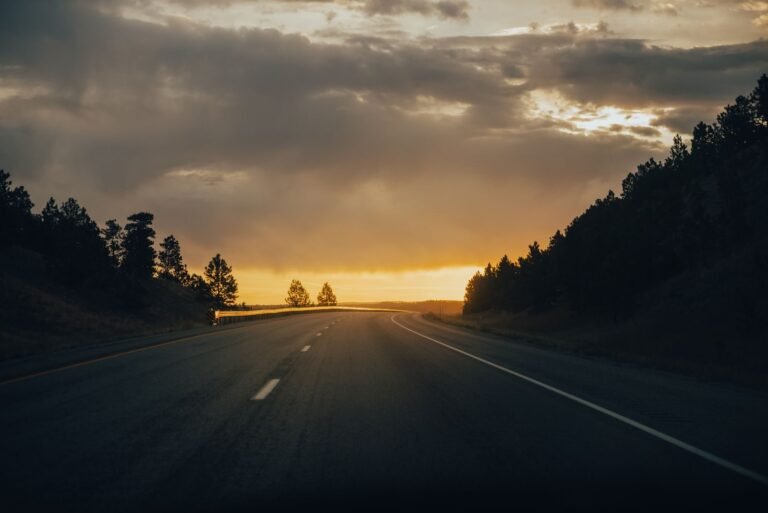 A peaceful highway winding through a forest under a dramatic sunset sky