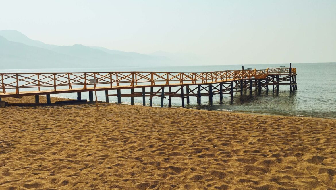 A tranquil scene of a wooden dock on a sandy beach reaching into the calm sea under a peac