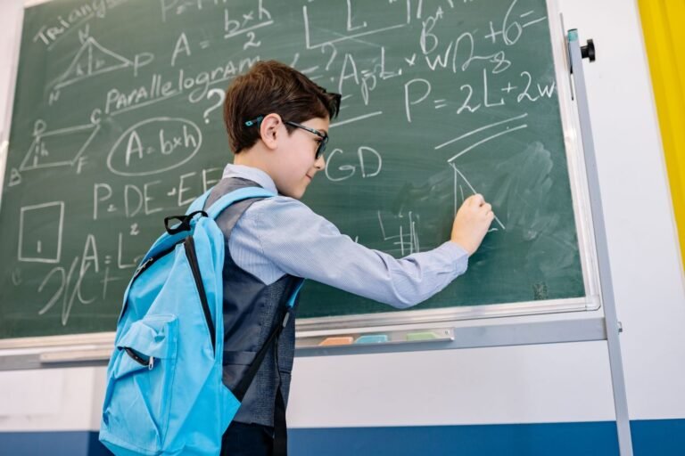 A young boy with glasses solving math equations on a classroom blackboard