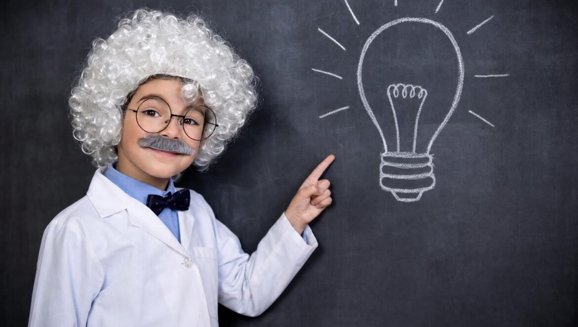 A boy in a white curly wig fake mustache and glasses dressed as a scientist pointing at a chalkdrawn light bulb on a blackboard | edCircuit A boy in a white curly wig fake mustache and glasses dressed as a scientist points at a chalk light bulb on a blackboard