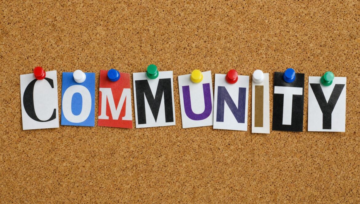 A cork board with the word COMMUNITY spelled out in mismatched cut out magazine letters fixed with colorful push pins