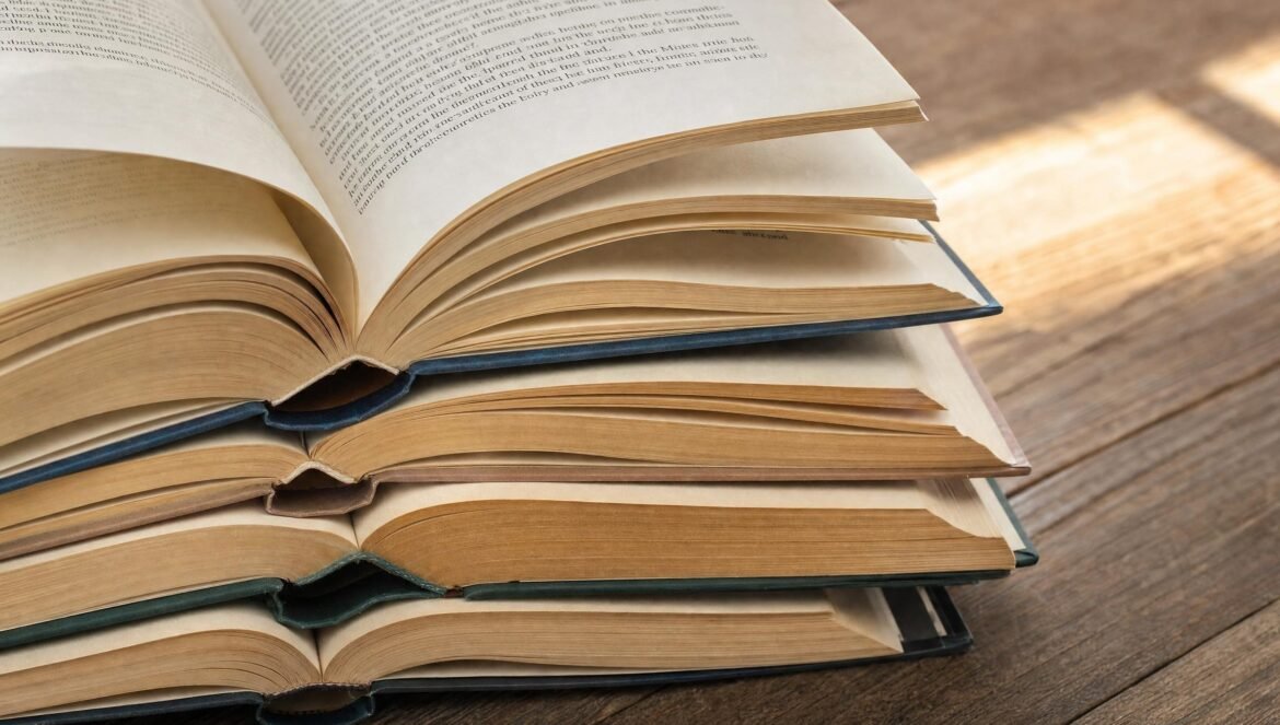 A stack of open books with pages fanned out on a wooden table warm light | edCircuit A stack of open books with pages fanned out on a wooden table warm light