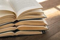 A stack of open books with pages fanned out on a wooden table, warm light