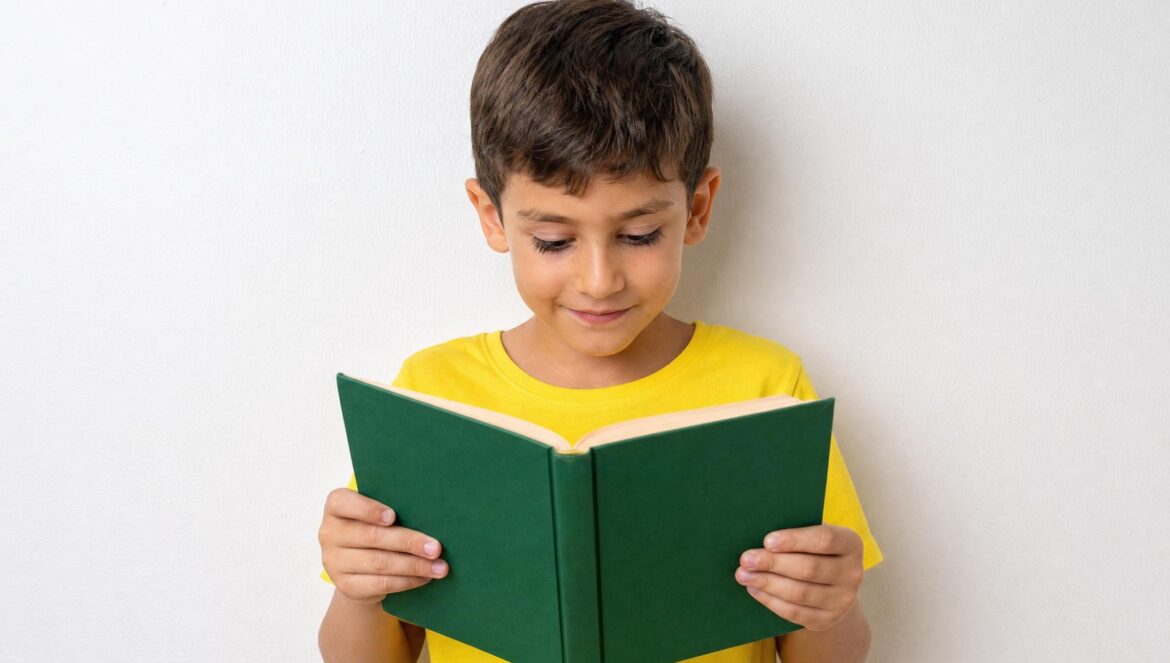 A young boy in a yellow shirt reading an open green book against a plain white wall | edCircuit A young boy in a yellow shirt reading an open green book against a plain white wall
