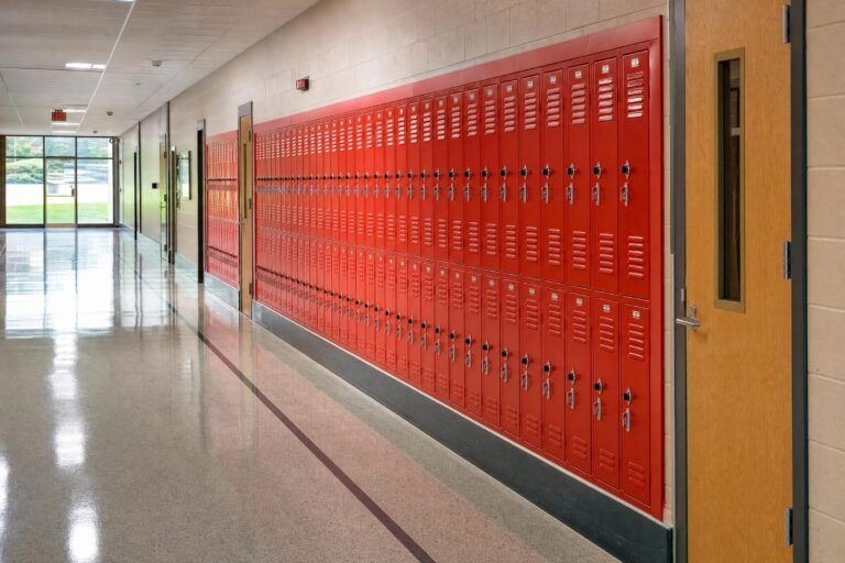 An empty school hallway with bright red lockers along one wall and wooden doors, polished floor, daylight