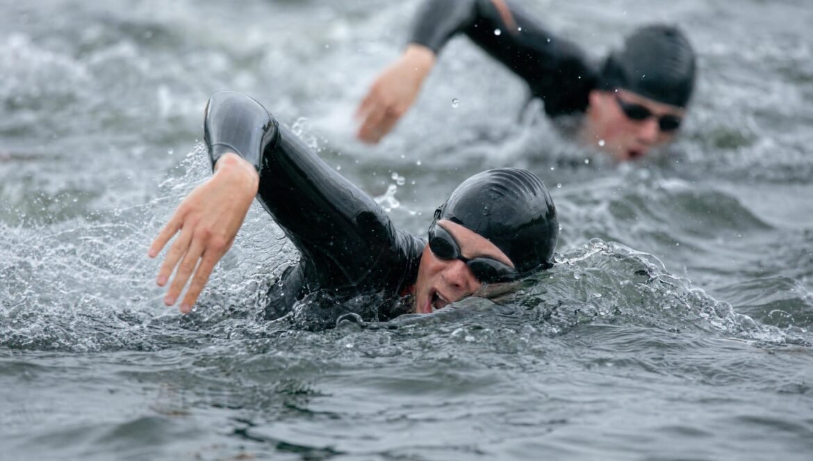 An openwater swimmer in a black swim cap and goggles midstroke in choppy grey water other swimmers behind splashes frozen in sharp detail | edCircuit An open water swimmer in a black swim cap and goggles mid stroke in choppy grey water other swimmers behind splashes frozen in sharp detail