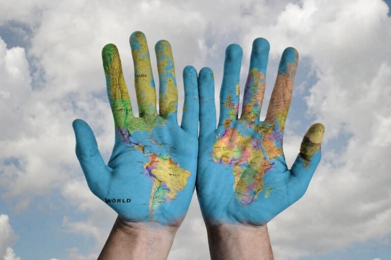 Two open human hands held up against a cloudy sky, painted with a colorful map of the world's continents and oceans