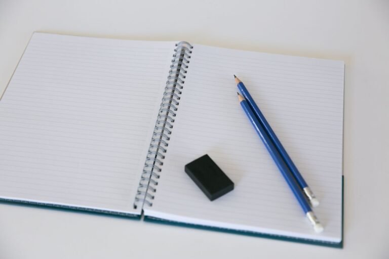 An open spiral notebook with two blue pencils and an eraser, ideal for students or artists
