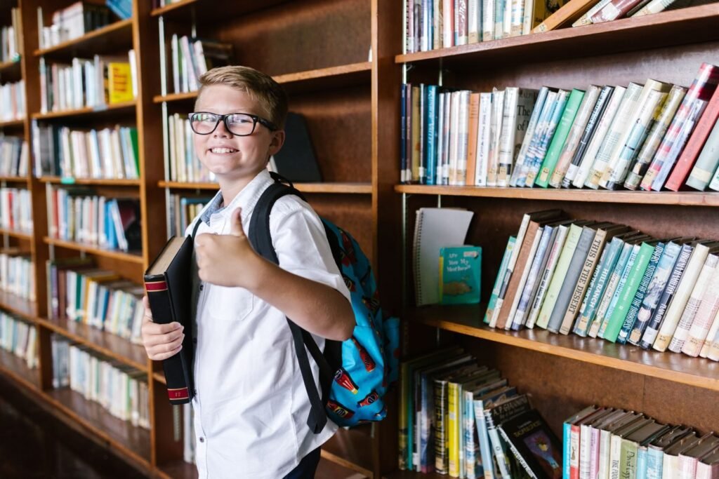 Young boy in a library giving a thumbs up while holding a book