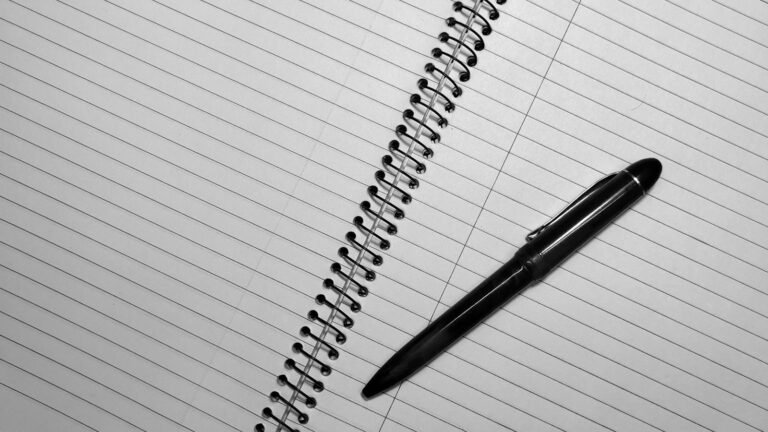 Close-up of a spiral notebook with black pen on lined pages, top view