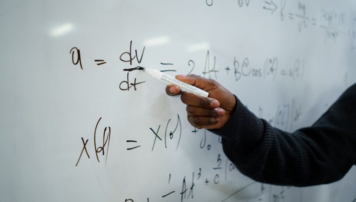 Close up of hand writing equations on a whiteboard in a classroom setting