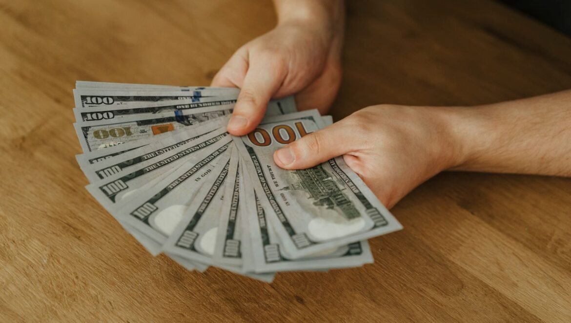 Close up of hands holding several 100 US dollar bills on a wooden surf