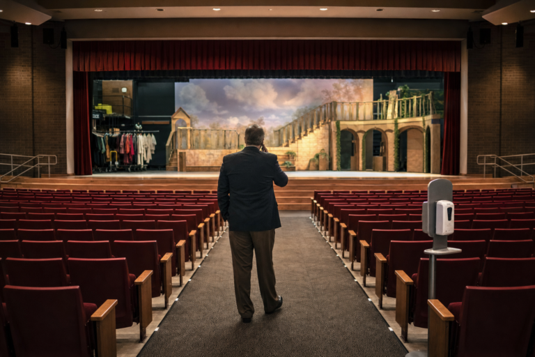 School crisis leadership in 2020: an administrator on the phone in an empty auditorium set for a cancelled school musical