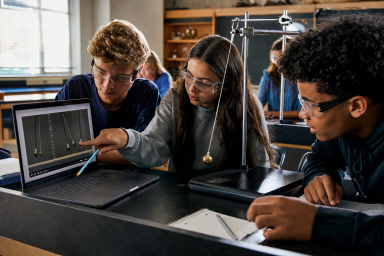 Students measuring a pendulum in a video on a laptop beside a real pendulum, interactive science