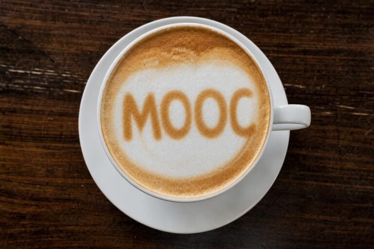 A cup of cappuccino on a white saucer seen from above with the milk foam art spelling MOOC, dark wooden table, soft cafe light
