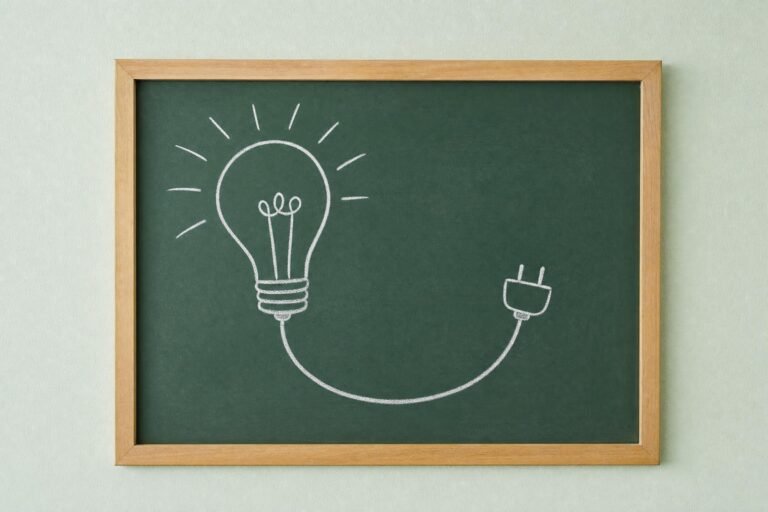 A framed green chalkboard on a pale mint wall with a simple chalk drawing of a light bulb whose cord ends in a plug, soft even light