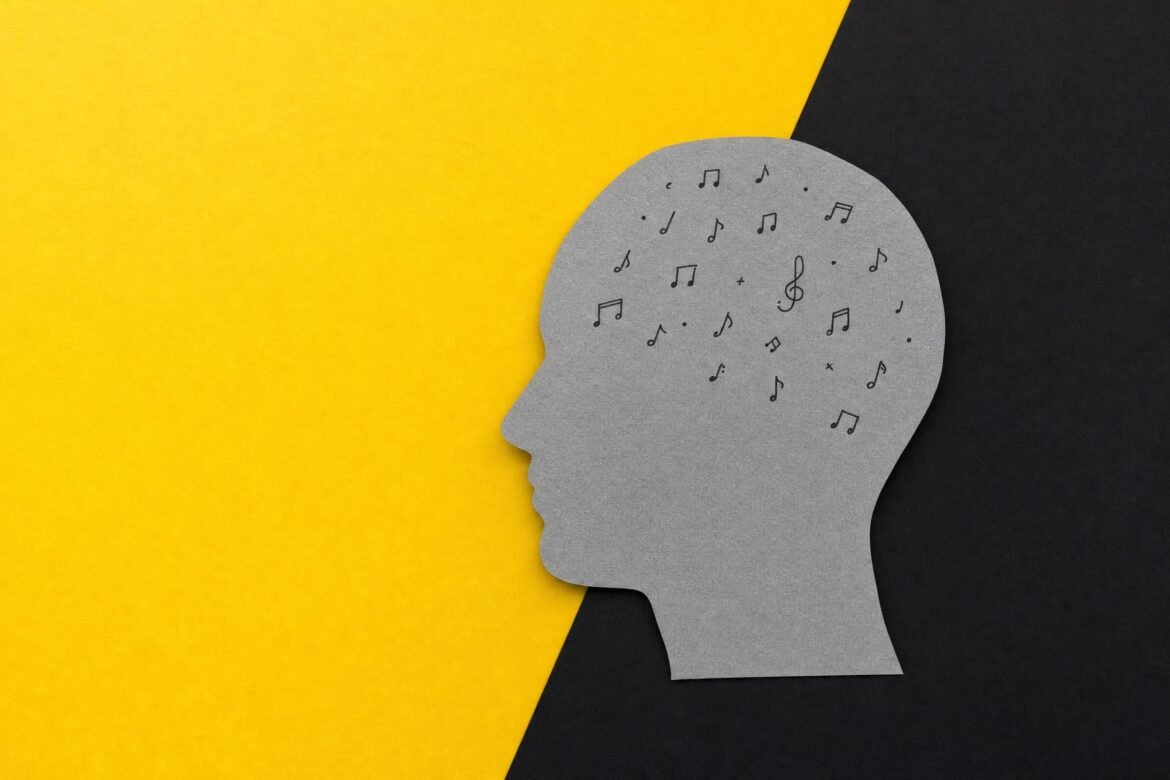 A gray paper cutout of a human head in profile with small music notes drawn inside the skull, on a bright yellow and black background