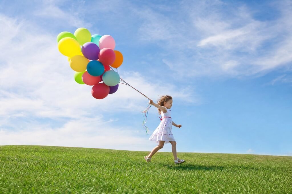 A little girl in a white dress running across a green grassy hill holding a big bunch of colorful balloons bright blue sky with wispy clouds | edCircuit A little girl in a white dress running across a green grassy hill holding a big bunch of colorful balloons bright blue sky with wispy clouds